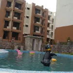 Swimming pool with inflatable toys surrounded by multi-storey 3BHK flats in Dehradun residential complex
